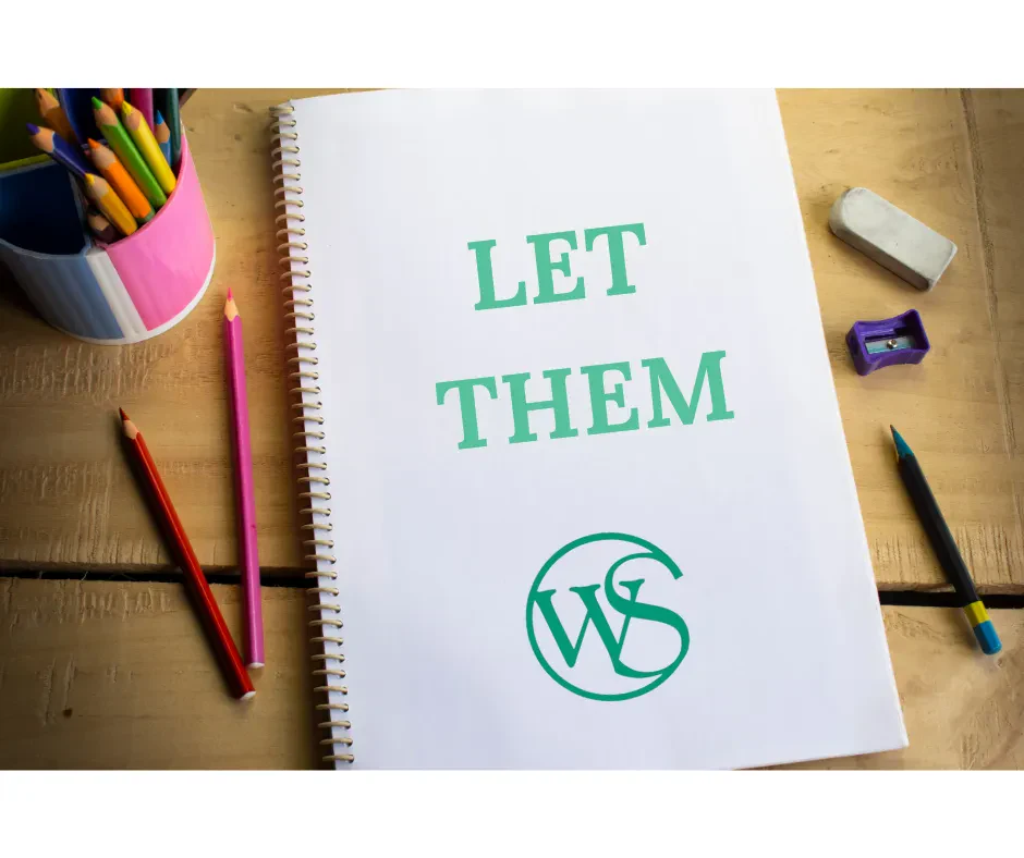 A flat lay photograph of a white spiral-bound notebook open on a light wooden desk, featuring the text "LET THEM" with the Wolf & Shore Law Group logo.