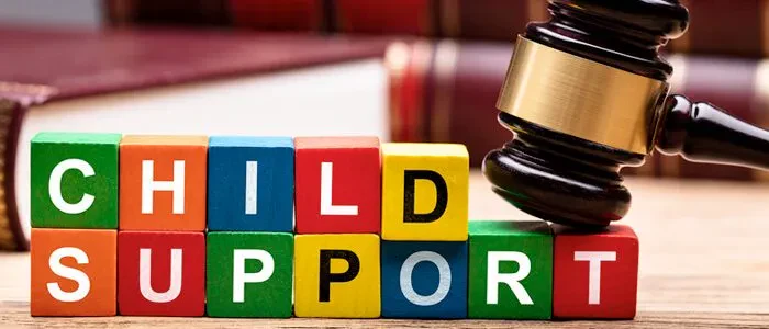 Colorful letter blocks spell CHILD SUPPORT next to a wooden judges gavel and law books, symbolizing legal matters related to child support.