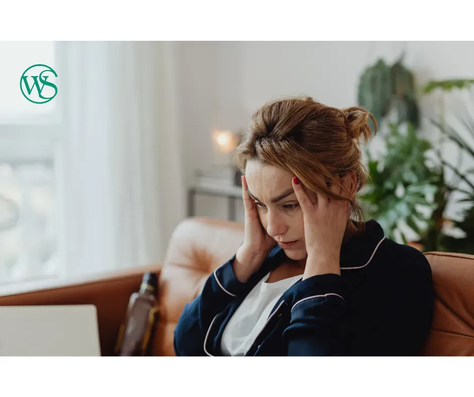 Stressed woman sitting on a couch, focused on her laptop, with a worried expression on her face.