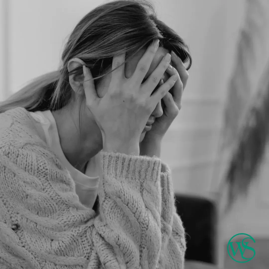 A person wearing a knit sweater sits with their face in their hands, appearing stressed or upset.